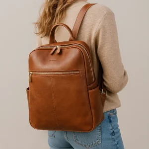 Woman wearing a stylish leather laptop backpack, walking through an urban setting with soft natural lighting and a modern, minimal outfit.