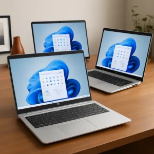 Three modern 17.3-inch HP laptops with silver finishes, open on a wooden desk, each displaying Windows 11 on their screens in a bright, minimalist workspace.