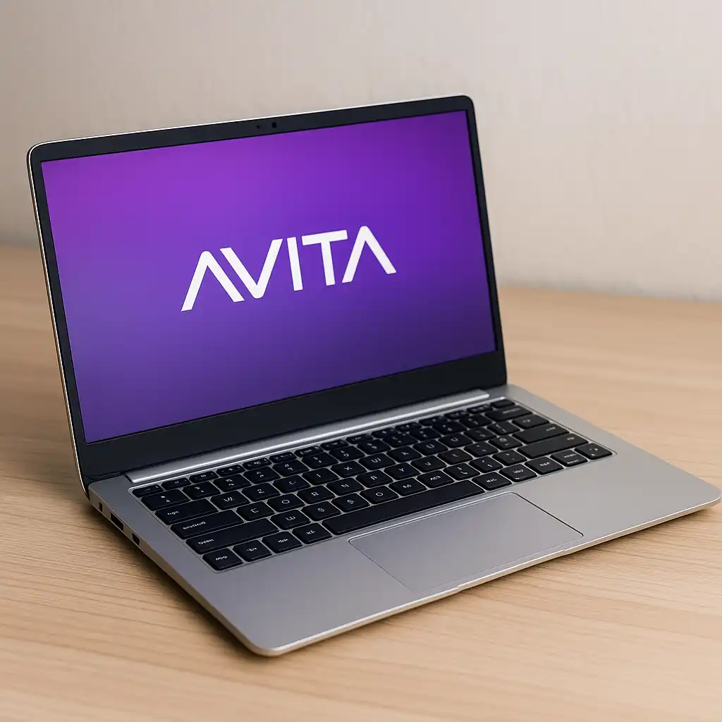 A silver AVITA laptop with a black chiclet keyboard displayed on a light wooden surface, showing the AVITA logo on its vibrant purple screen.